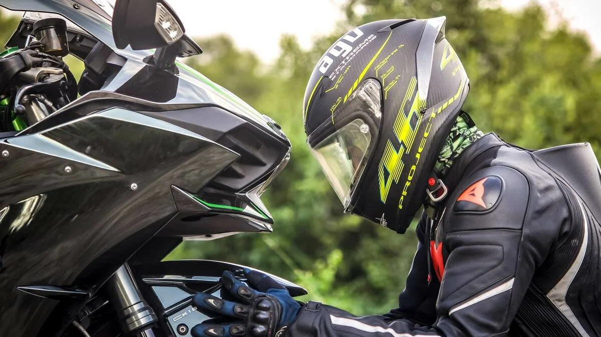 Motoqueiro com roupa e capacete preto olhando a roda da moto