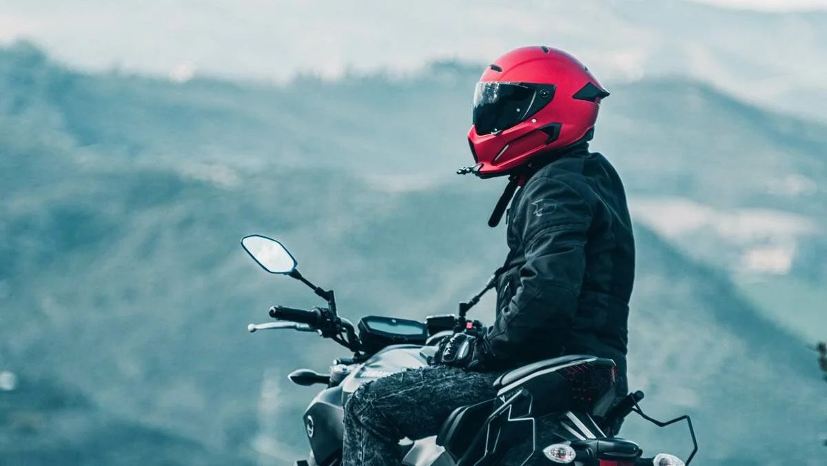 Motoqueiro de roupa preta e capacete vermelho olhando a paisagem