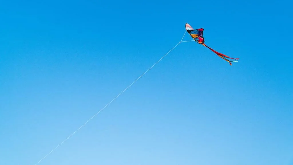 Foto de uma pipa colorida voando em um céu azul sem nuvens