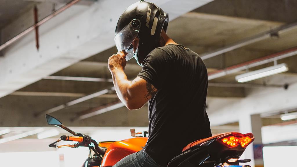 motoqueiro abaixando a viseira do capacete em cima de moto laranja e usando camiseta de manga curta preta