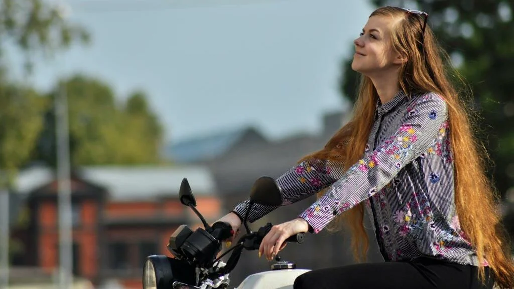 mulher ruiva montada na moto, sorrindo e olhando para cima