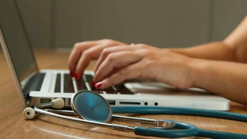 Pessoa digitando em um computador com um estetoscópio ao lado