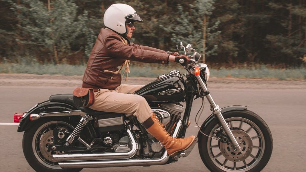 motoqueiro com roupa marrom e capacete aberto branco pilotando em estrada