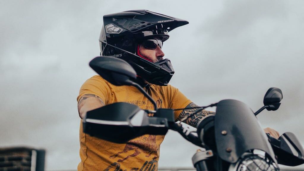 Motoqueiro usando capacete de motocross preto e camisa laranja, montado em uma moto preta