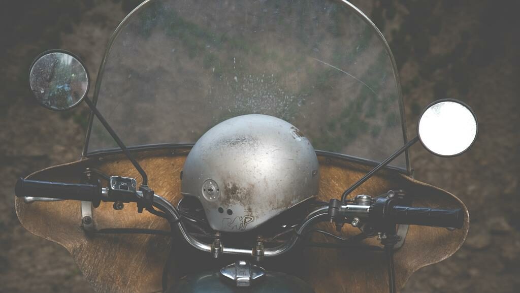 capacete aberto, prata, em cima do guidão de uma scooter