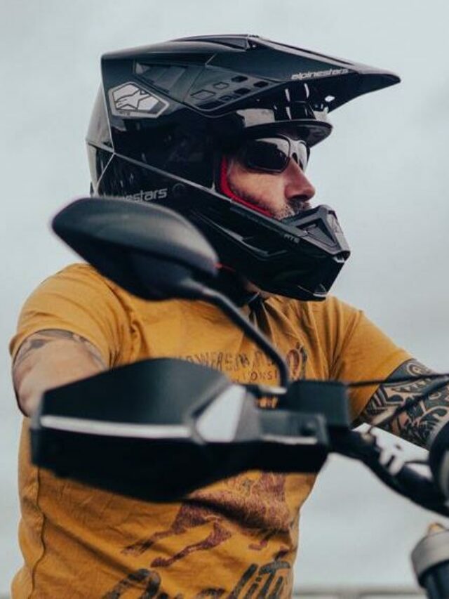 Motoqueiro usando capacete de motocross preto e camisa laranja, montado em uma moto preta