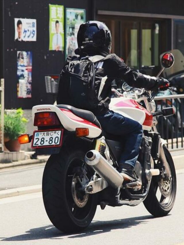 Motoqueiro com roupa preta em cima de moto branca e vermelha, em um dia de muito sol