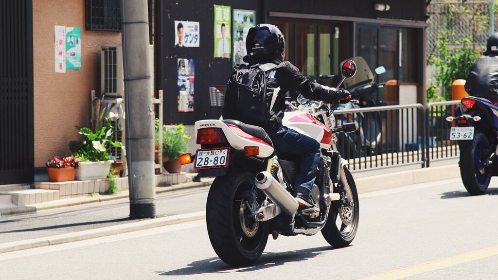 Motoqueiro com roupa preta em cima de moto branca e vermelha, em um dia de muito sol