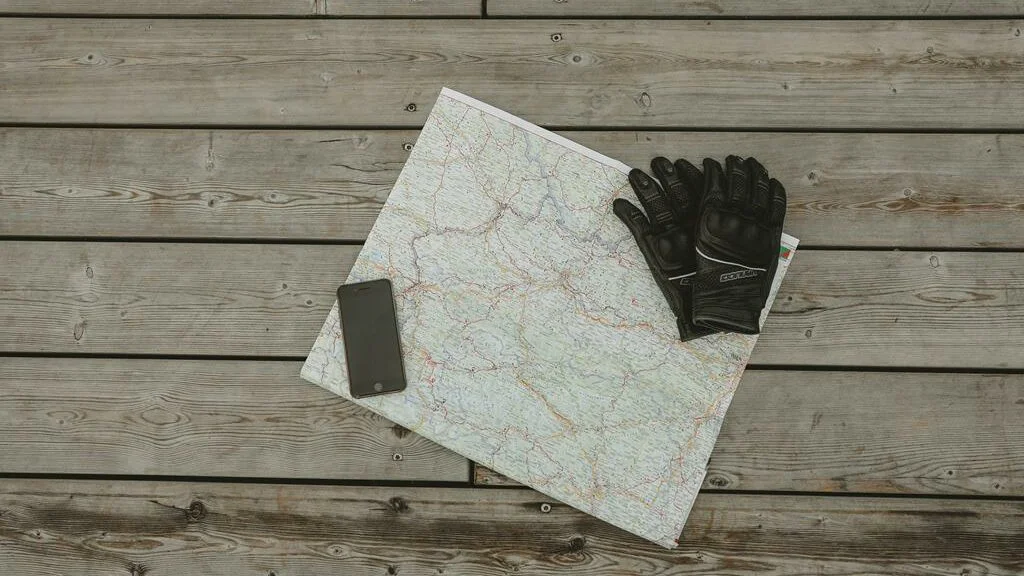 Luva preta e telefone celular, em cima de um mapa branco.