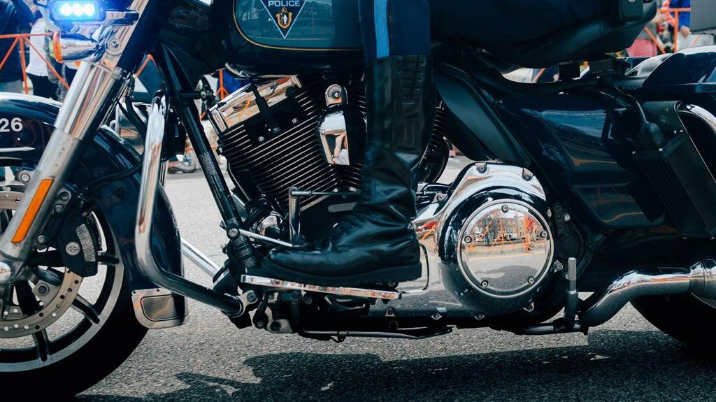 bota de motoqueiro preta no pedal de uma moto prata e escura da polícia