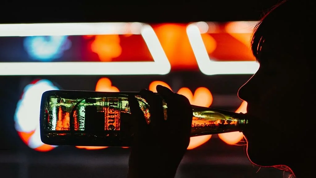 Pessoa bebendo uma cerveja em garrafa com luzes da policia