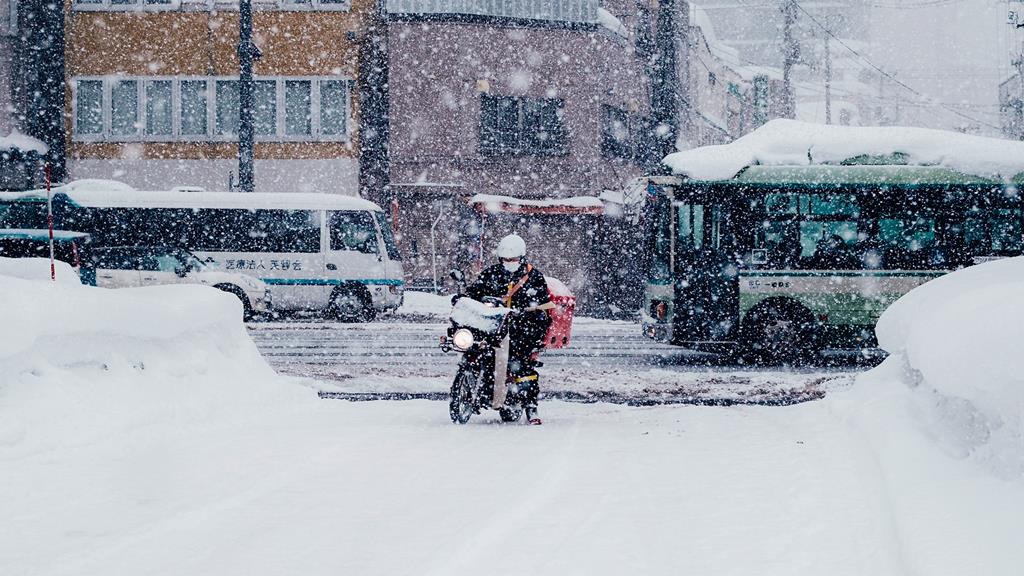 motoqueiro pilotando moto e entrando em rua com muita neve caindo